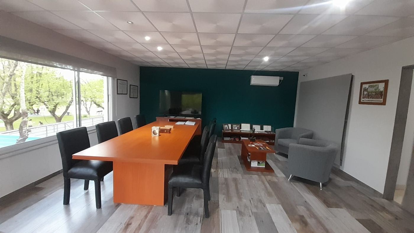 Sala de reuniones con mesa para diez personas, pantalla y ventanales hacia la plaza